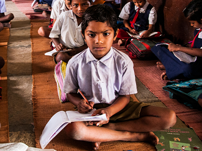 Children sitting on the floor in a classroom setting, engaged in learning activities.